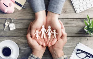 Mani proteggono una famiglia di carta su tavolo